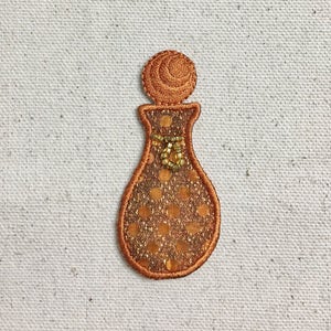 May include: A small, orange, embroidered perfume bottle with a gold polka dot pattern and a gold bow.