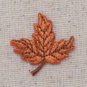 Puede incluir: Una pequeña aplicación de hoja de arce bordada de color naranja. La hoja está detallada con costuras y tiene un tallo.