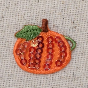 Peut inclure: Un écusson en forme de citrouille orange avec une feuille verte et une tige marron. La citrouille est ornée de paillettes orange. L'écusson est probablement destiné à la décoration, peut-être pour les vêtements ou l'artisanat.