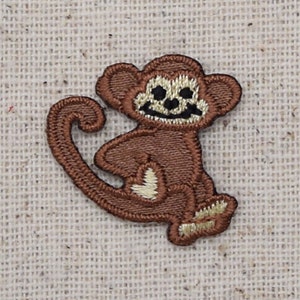 Puede incluir: Una aplicación de mono bordada en marrón con una cara sonriente. El mono está sentado con la cola enroscada alrededor de su cuerpo.