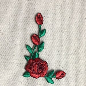 May include: Red embroidered rose flower applique with green leaves. The rose is in a corner design with a large rose and smaller buds.
