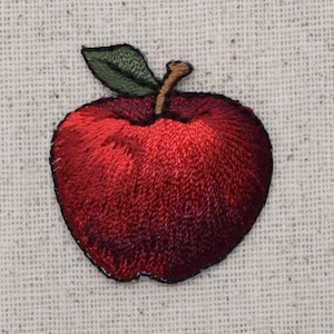 Pode incluir: Maçã vermelha bordada com uma folha e um caule verdes. A maçã está sobre um fundo de tecido bege.