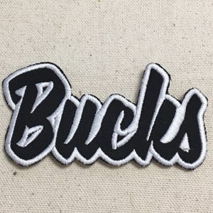 May include: Black and white embroidered patch with the word "Bucks" in a stylized font.