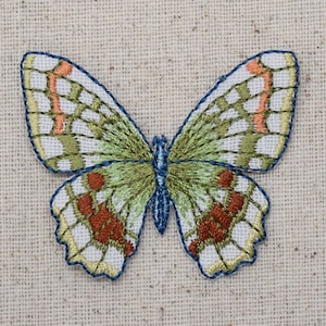 May include: A green and white embroidered butterfly with orange accents on a beige fabric background.