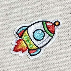 Könnte beinhalten: Ein bunter gestickter Bügelaufkleber mit einem Cartoon-Raketenschiff mit einer rot, gelb, grün und blauen Flamme.