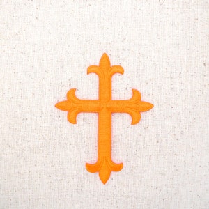 Könnte beinhalten: Orange gestickte Kreuz mit einem dekorativen Design auf einem weißen Stoffhintergrund.