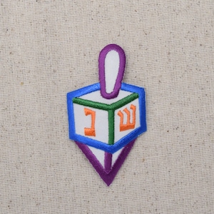 May include: A blue, green, white, and purple felt dreidel with the Hebrew letters Nun, Gimel, Hey, and Shin embroidered on the sides.