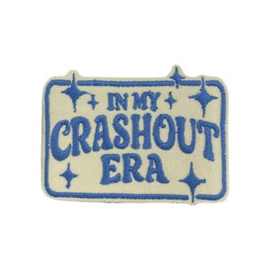 Puede incluir: Parche rectangular con texto azul "IN MY CRASHOUT ERA" sobre fondo crema. Borde azul y detalles de estrellas. Ideal para personalizar ropa y accesorios.