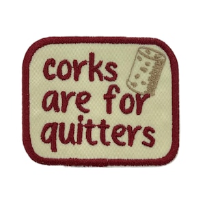May include: Embroidered patch with a cream background and a burgundy border. The patch features the phrase "corks are for quitters" in burgundy lettering, along with an illustration of a cork.