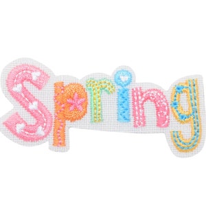Puede incluir: Parche bordado con la palabra "Spring" en letras de colores. Las letras están delineadas en blanco y tienen una variedad de pequeños detalles, incluidos corazones y estrellas.