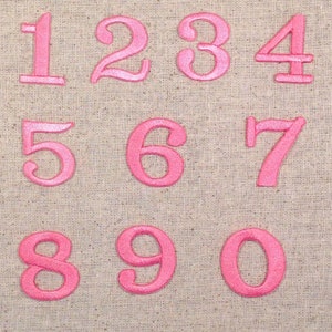 May include: Pink felt numbers 1 to 0 on a beige fabric background.