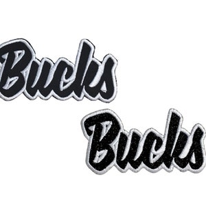 May include: Two black embroidered patches with the word "Bucks" in a stylized font. The patches have a white outline.