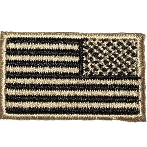 Può includere: Un piccolo patch ricamato della bandiera americana con uno sfondo beige e cuciture nere. La bandiera è nel design tradizionale con 13 strisce e 50 stelle.