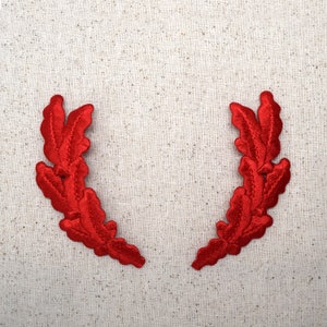 May include: Two red fabric laurel wreaths on a beige linen background.