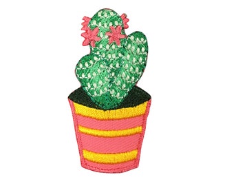 Könnte beinhalten: Ein grüner Kaktus mit rosa Blüten in einem rosa und gelben Topf. Der Kaktus ist auf einem Stoffpatch gestickt.