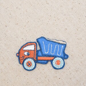 May include: A blue and orange embroidered patch of a cartoon dump truck. The truck has a smiling face and a blue bed with white lines.