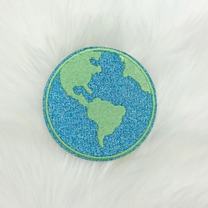 May include: A round, embroidered patch featuring a stylized depiction of Earth. The continents are rendered in light green against a sparkling blue background, with a matching green border. The patch is designed to be sewn or ironed onto fabric.