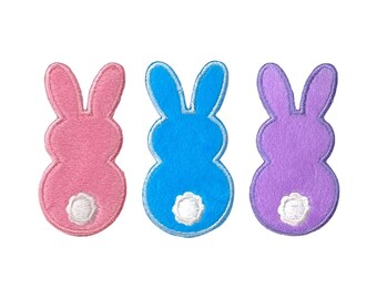 May include: Three felt bunny rabbit patches in pink, blue, and purple. Each bunny has a white fluffy tail.