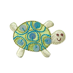 May include: A green and blue embroidered turtle applique with a smiling face. The turtle has a light green shell with blue swirls and blue sequins.