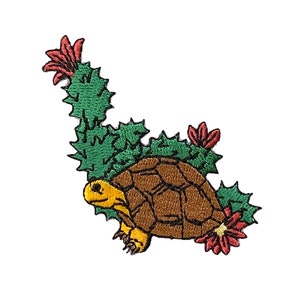 May include: An embroidered patch featuring a brown turtle with a yellow head and legs, partially hidden behind a green cactus with red flowers.