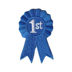 May include: A blue embroidered patch in the shape of a first-place award ribbon. The circular center features the white stitched text 1st, surrounded by a pleated border and two downward-pointing ribbon tails with pointed ends.