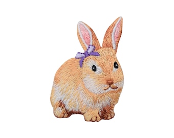 May include: A brown embroidered bunny with a purple bow. The bunny is sitting on a white background.