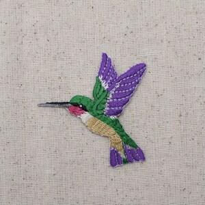 Puede incluir: Parche bordado de colibrí morado y verde. El colibrí está en vuelo con las alas extendidas. El parche es perfecto para agregar un toque de naturaleza a tu ropa o accesorios.