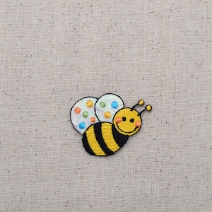 May include: An embroidered bee with yellow and black stripes, white wings and colourful polka dots. The bee has a smiling face.