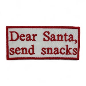 May include: Embroidered patch with a white background and a red border. The text "Dear Santa, send snacks" is stitched in red thread. The patch is rectangular.