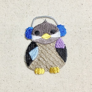 May include: Embroidered patch of a brown penguin wearing blue earmuffs. The penguin has a yellow beak and feet.