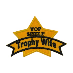 May include: Embroidered patch in a star shape with the words "TOP SHELF" above a banner that reads "Trophy Wife". The star and banner are yellow with black text and trim.
