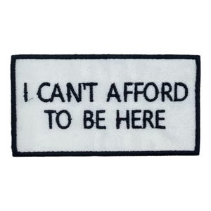 Puede incluir: Un parche rectangular blanco con texto negro que dice "I CAN'T AFFORD TO BE HERE". El parche tiene un borde negro. El texto está en negrita, con una fuente sans-serif.