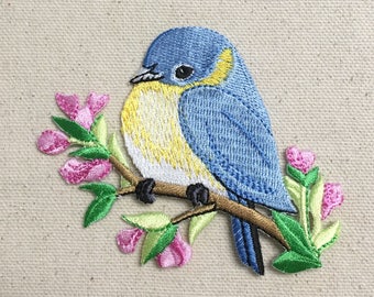 Può includere: Toppa ricamata da stirare con un passero azzurro appollaiato su un ramo con fiori rosa. L'uccello ha il petto giallo e la testa blu.