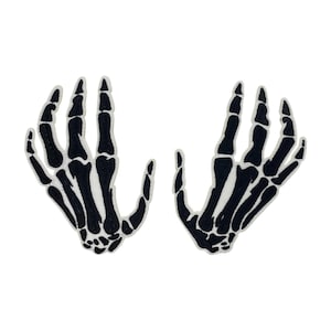 Könnte beinhalten: Zwei schwarze gestickte Skelett-Hand-Patches. Die Hände sind in einer erhobenen Position mit gespreizten Fingern.