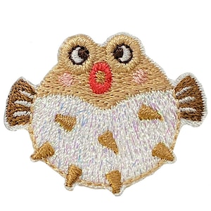 May include: An embroidered pufferfish patch in brown and white with a red mouth and black eyes. The pufferfish is set against a white background.