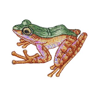 Pode incluir: Um remendo bordado de um sapo verde e castanho com a parte inferior de cor púrpura clara. O sapo está em posição de salto com as pernas estendidas.