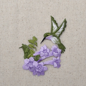 May include: Embroidered patch featuring a green hummingbird with white accents hovering over a cluster of purple flowers with green leaves.