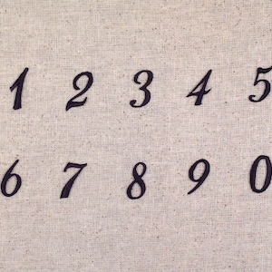 May include: Black embroidered numbers 1 through 0 on a beige fabric background.