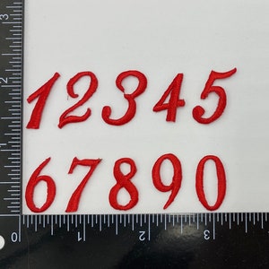 May include: Red felt numbers 1 through 10, in a cursive font, are arranged in two rows on a white background. The numbers are approximately 1 inch tall.