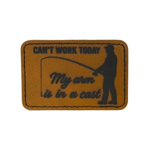 May include: A rectangular, brown patch with a black border. The patch features the text "CAN'T WORK TODAY" above the words "My arm is in a cast." A silhouette of a person fishing is on the right side of the patch.