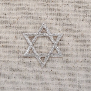 May include: A silver Star of David on a beige fabric background.