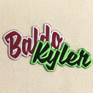 May include: Two embroidered patches with names. The first patch is red with white outline and says "Baldo". The second patch is green with black outline and says "Kyler".