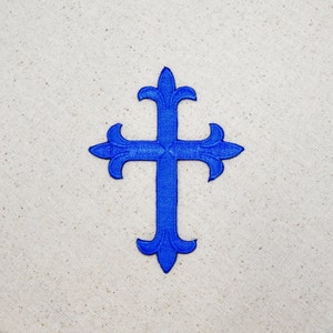 May include: A blue cross with a decorative design. The cross is made of fabric and has a slightly raised texture.