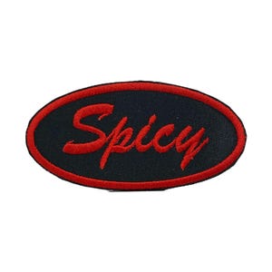 Op de afbeelding: Zwart ovaalvormig embleem met het woord "Spicy" geborduurd in rood script. De patch heeft een rode rand. Deze patch is geschikt voor jassen, tassen of andere kledingstukken. De achtergrond is wit.