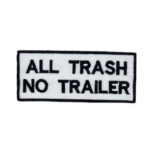 May include: A rectangular patch with the text "ALL TRASH NO TRAILER" embroidered in black on a white background. The patch has a black border and is likely designed to be sewn or ironed onto clothing or accessories.