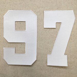 May include: White felt fabric numbers 97, commonly used for sports jerseys or team apparel.