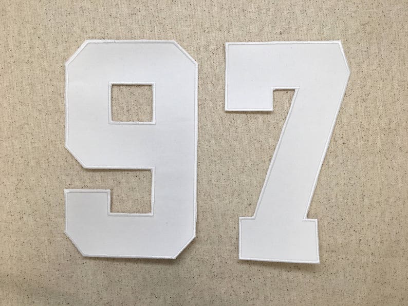 May include: White felt fabric numbers 97, commonly used for sports jerseys or team apparel.