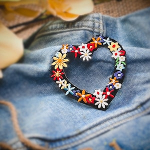 以下が含まれることがあります： デニムの背景にカラフルな花が刺繍されたハート型のワッペン
