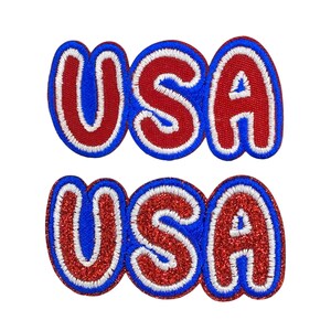 May include: Two embroidered patches spelling "USA". The top patch features red letters with a blue outline and a white border. The bottom patch has red glitter letters with a blue outline and a white border. Both patches are set against a white backdrop.