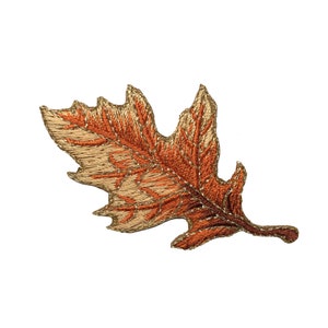 May include: A gold and orange embroidered leaf applique. The leaf is detailed with stitching and has a slightly textured surface.